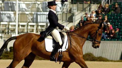 Allie Knowles riding a bay horse in a dressage competition wearing a top hat and tails.