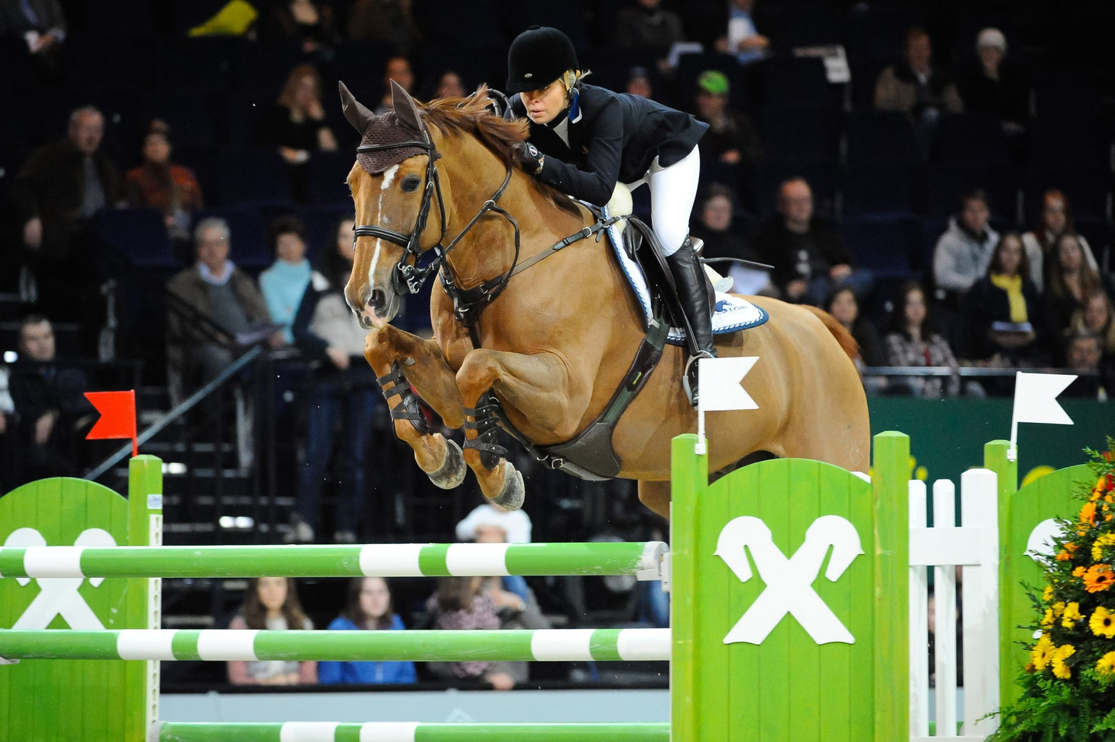 Edwina Alexander riding a chestnut horse over a vertical in a show jumping competition