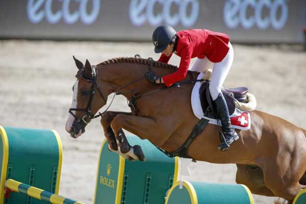 Janika Sprunger riding a bay horse over an oxer.