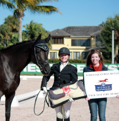 Photo of Jules Anderson standing next to her black horse and the rep from World Equestrian Brands with their prize package