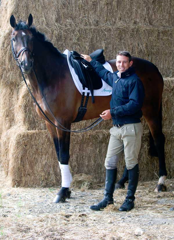 Sam Griffiths standing next to a dark bay horse in dressage equipment and attire.