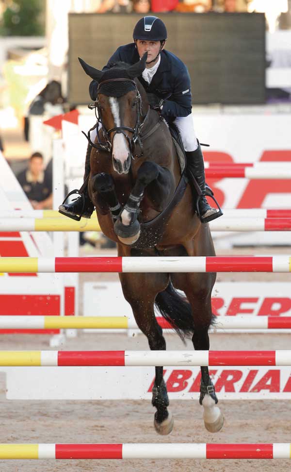 Billy Twomey riding a dark bay horse over a large vertical.