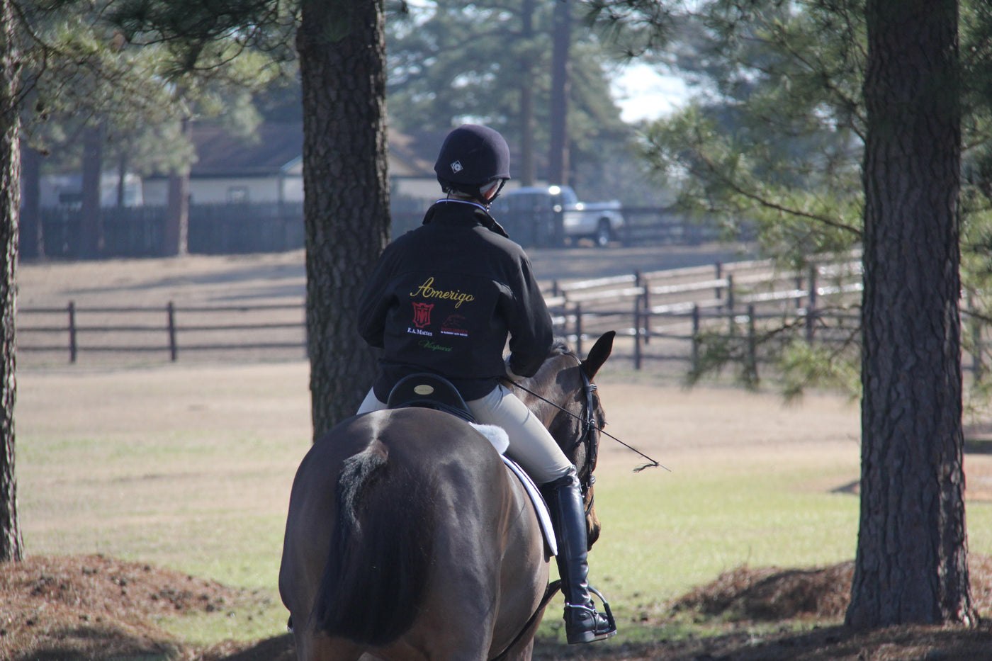 Sponsored rider riding a dark bay horse away from us wearing a logo'd jacket.